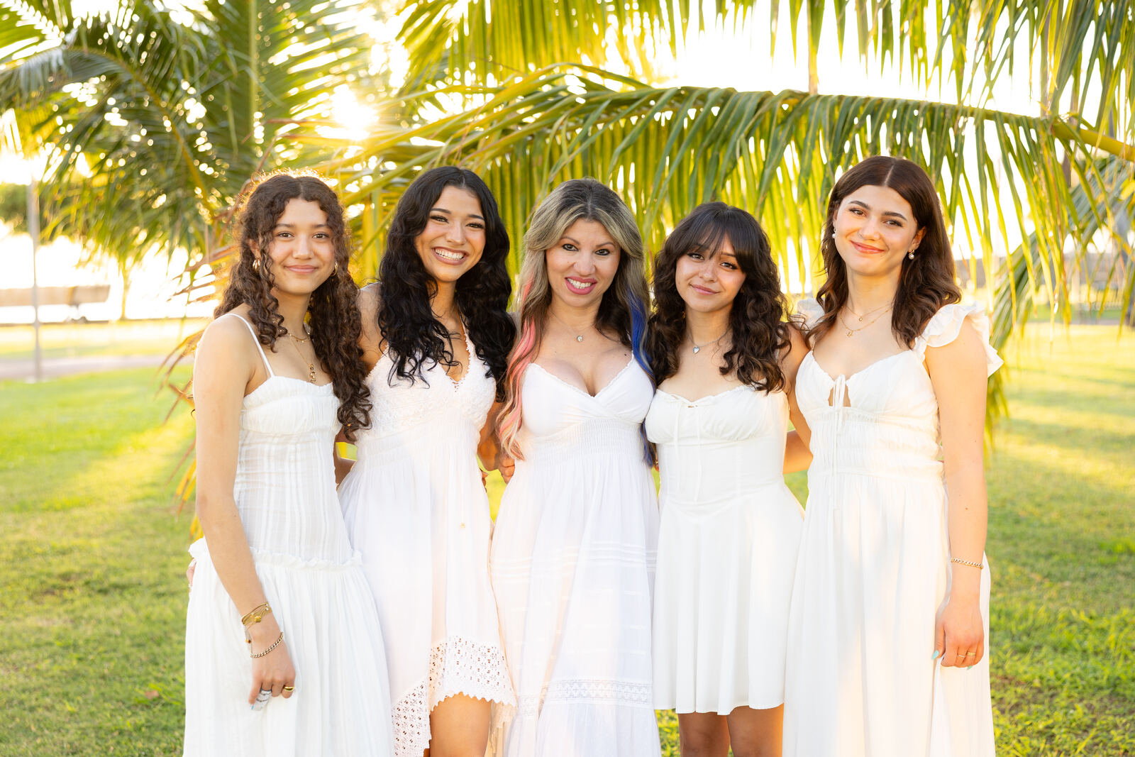 Mother and daughters laughing under a palm tree at sunset