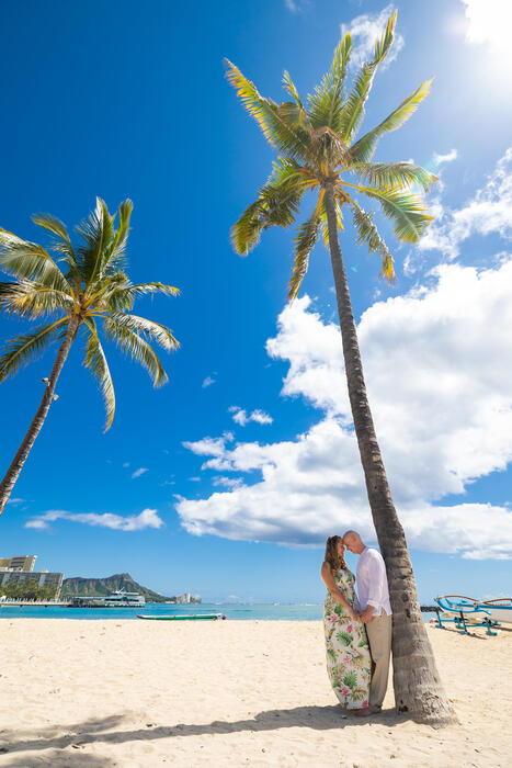 Couple embracing under a palm tree with Diamond Head behind them