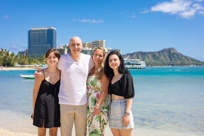 Family of four standing on Waikiki Beach with Diamond Head behind them