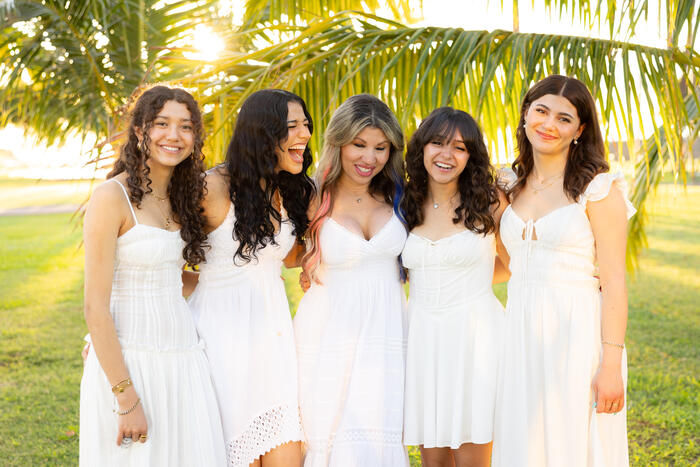Mother and four daughters laughing under a palm tree at golden hour