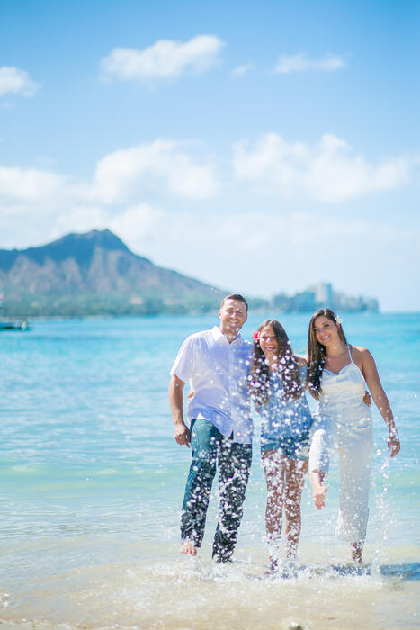 Three family members walking through shallow water with Diamond Head behind them