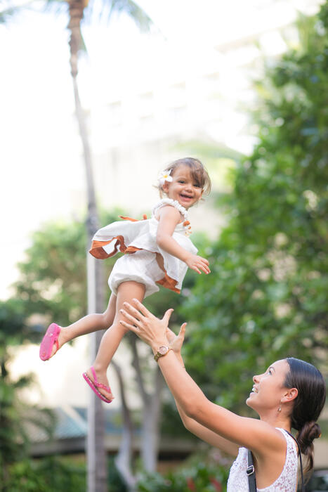 Mother tossing a laughing toddler into the air in a garden